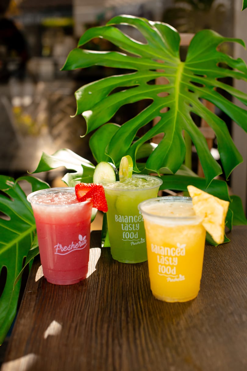 Three colorful Fresheria drinks: red with strawberry, green with cucumber and lime, and yellow with pineapple.